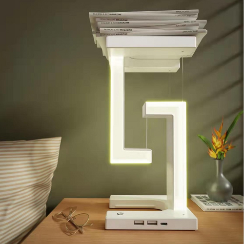 Modern LED desk lamp on a wooden surface with magazines stacked on top, in a room setting.